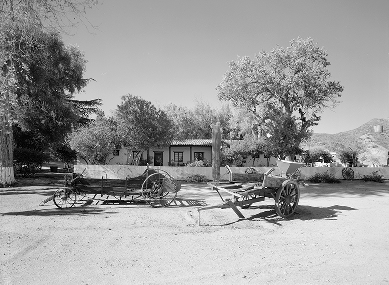 GENERAL VIEW OF HOUSE, GARDEN AND FENCE, WITH OLD FARM EQUIPMENT NEAR DRIVEWAY; CAMERA FACING WEST 